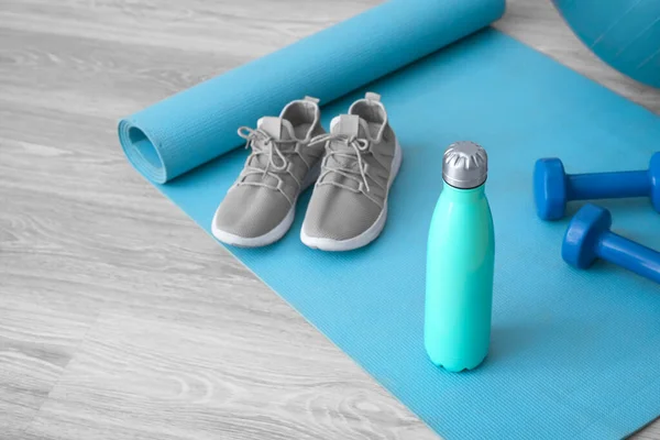 Sports water bottle with equipment and sneakers on mat