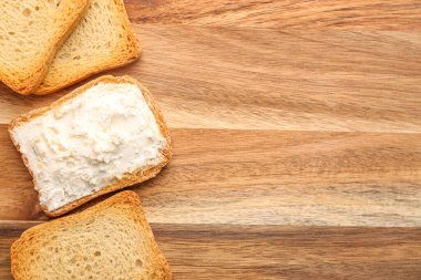 Toasts with tasty cream cheese on wooden background