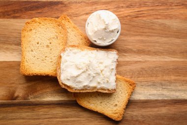 Toasts with tasty cream cheese on wooden background