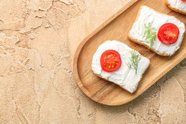 Wooden board of tasty bread rusks with cream cheese and tomatoes on color background