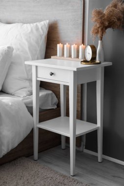 Vase with pampas grass, alarm clock and candles on table in bedroom