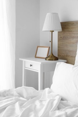 Blank photo frame and lamp on table in light bedroom