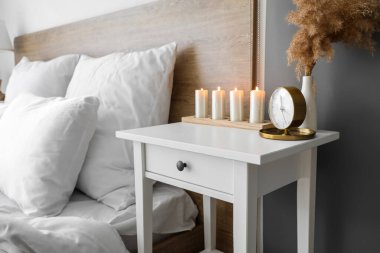 Vase with pampas grass, alarm clock and candles on table in bedroom