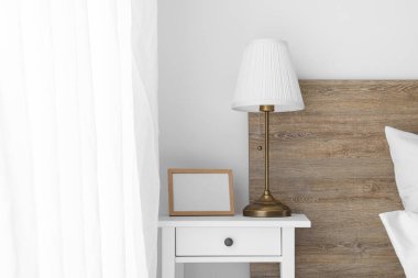 Blank photo frame and lamp on table in light bedroom
