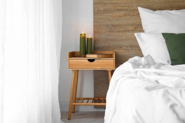 Burning candles and book on wooden table in bedroom