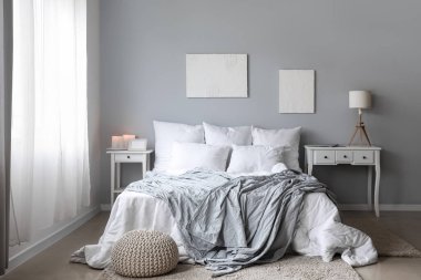 Interior of light bedroom with tables, big bed and paintings