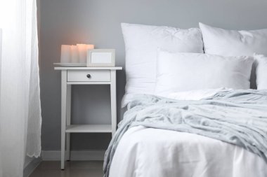 Blank photo frame with burning candles on table in light bedroom