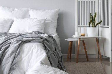 Bedside tables with houseplant and cup in light bedroom