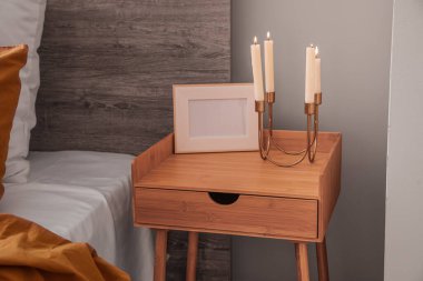Wooden bedside table with frame and candles in bedroom