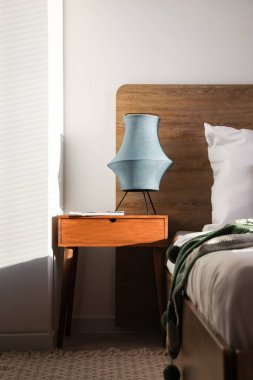 Wooden bedside table with lamp and magazine in bedroom