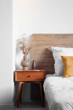 Vases with dry reeds and mobile phone on wooden table in bedroom