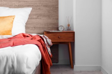 Wooden table with magazine, alarm clock and reed diffuser in bedroom