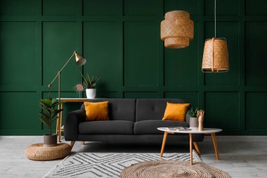 Interior of living room with black sofa, table and houseplants near green wall