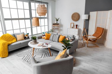 Beautiful interior of living room with cozy grey sofas, armchair and table near window