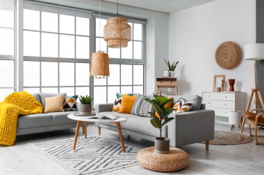 Beautiful interior of living room with cozy grey sofas, table and houseplants near window