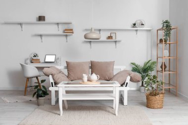 Stylish interior of living room with cozy sofa, teapot and cups on table