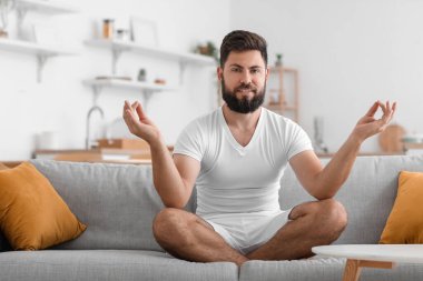 Handsome young man meditating on sofa at home