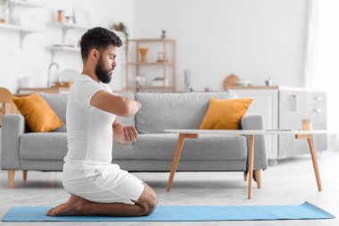 Handsome young man meditating on mat at home