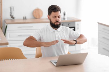 Handsome young man meditating at table in kitchen