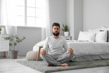 Handsome young man meditating on carpet at home