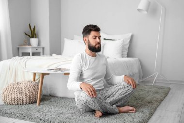 Handsome young man meditating on carpet at home