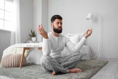 Handsome young man meditating on carpet at home