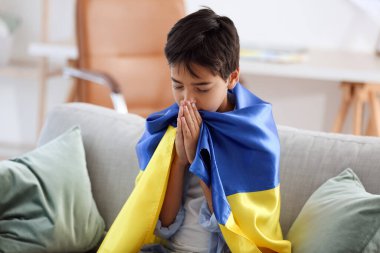 Little boy with flag of Ukraine praying at home
