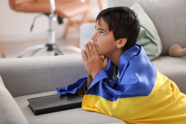 Little boy with flag of Ukraine praying at home