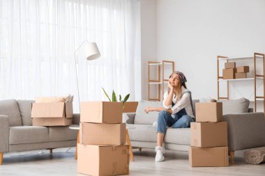 Dreaming young woman sitting on sofa in living room on moving day