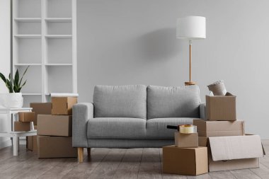 Cardboard boxes with grey sofa and lamp in living room on moving day