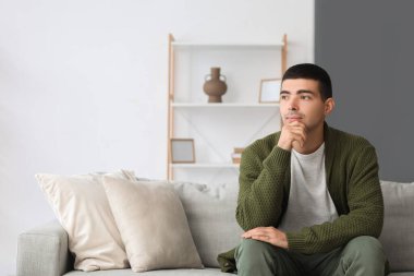 Evdeki kanepede oturan düşünceli genç adam.