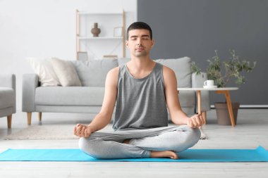 Young man meditating on mat at home