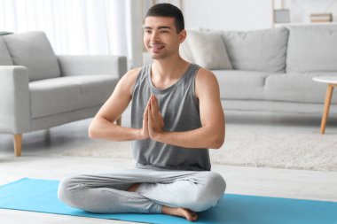 Young man meditating on mat at home
