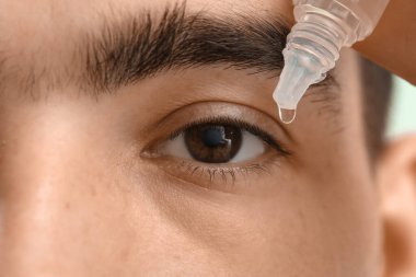 Young man with eye drops on green background, closeup