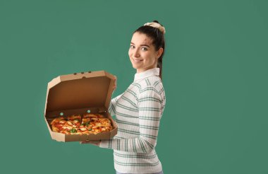 Yeşil arka planda bir kutu lezzetli pizzası olan genç kadın.