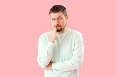 Pembe arka planda tırnaklarını yiyen yakışıklı bir adam.