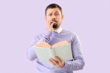 Handsome man with book biting nails on lilac background