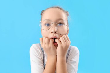 Stressed little girl biting nails on blue background