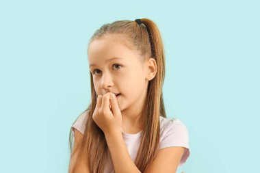 Little girl biting nails on blue background, closeup