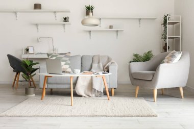Cozy interior of living room with grey sofa, armchair and modern laptop on table