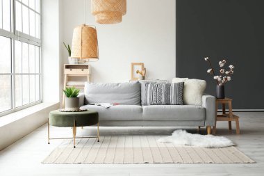 Cozy interior of living room with grey sofa, pouf and fur carpet near window