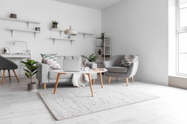 Cozy interior of living room with grey sofa, armchair and modern laptop on table