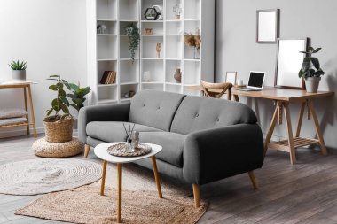 Stylish interior of living room with grey sofa, table and wicker pouf