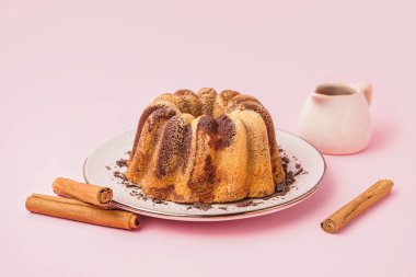 Plate with delicious cake and cinnamon on pink background