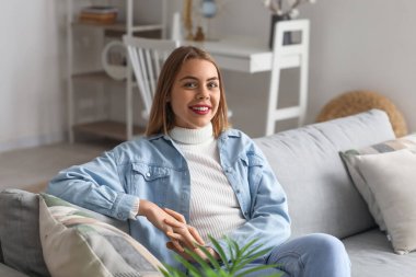 Young woman sitting on grey couch at home