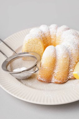 Plate with delicious cake and sieve of powdered sugar on white background