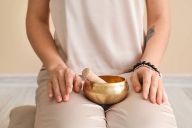Beautiful meditating young woman with Tibetan singing bowl at home, closeup
