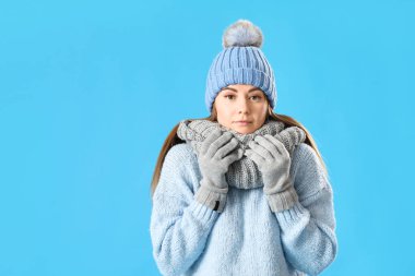 Frozen young woman in winter clothes on blue background