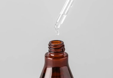 Dripping of serum into bottle on light background, closeup