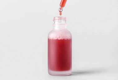 Dripping of healthy serum into bottle on light background